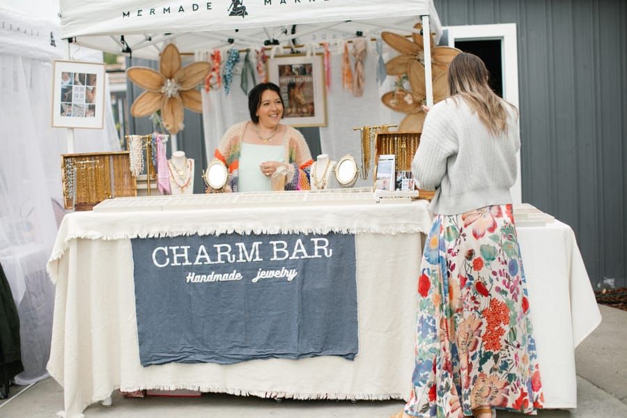 A maker serving a shopper at the Charm Bar under a Mermade tent